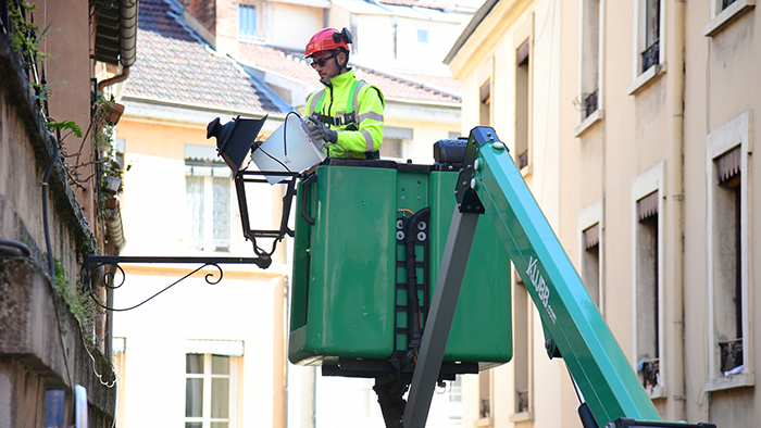 Technicien dans la nacelle d'une grue en train de changer l'ampoule d'un réverbère