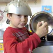 Enfant cuisinant de manière un peu chaotique avec une passoire sur la tête